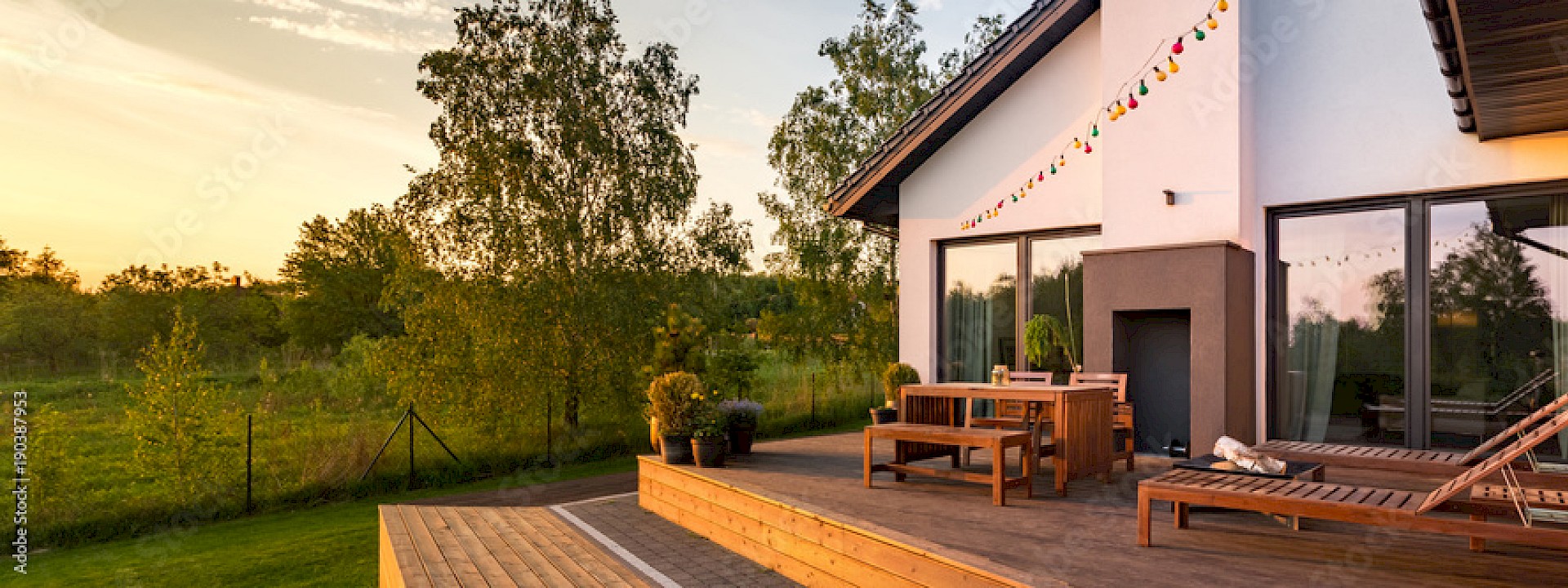 Haus mit Terrasse, Gartenmöbeln und Lichterkette bei Sonnenuntergang.